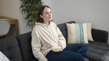 Young blonde woman watching movie sitting on sofa at home