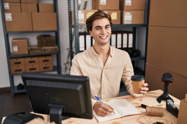 Young caucasian man ecommerce business worker writing on notebook drinking coffee at office