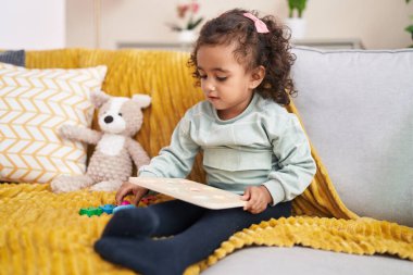 Adorable hispanic girl playing maths game sitting on sofa at home