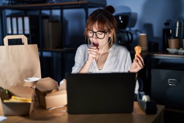 Young beautiful woman working using computer laptop and eating delivery food feeling unwell and coughing as symptom for cold or bronchitis. health care concept. 