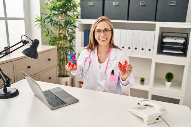 Genç sarışın kardiyolog klinikte anatomik kalp modeli tutuyor.