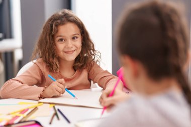 Two kids students sitting on table drawing on notebook paper at classroom