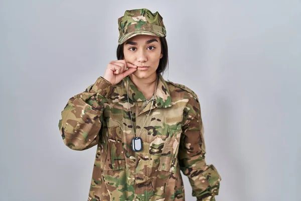 Young south asian woman wearing camouflage army uniform mouth and lips shut as zip with fingers. secret and silent, taboo talking