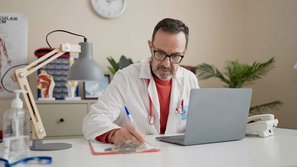 Klinikteki Belgelerde Dizüstü Bilgisayar Kullanan Orta Yaşlı Bir Doktor — Stok fotoğraf