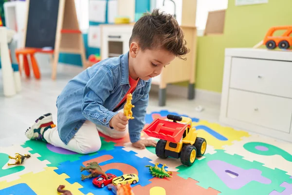 愛らしいヒスパニック幼児遊びとともにトラクターとディノおもちゃ座っています床に幼稚園 — ストック写真