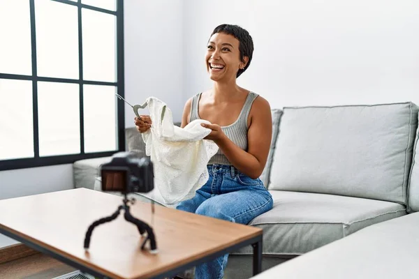 Young hispanic woman smiling confident sending clothes at home