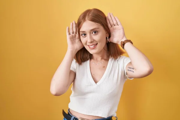 Mujer Pelirroja Joven Pie Sobre Fondo Amarillo Tratando Escuchar Ambas — Foto de Stock