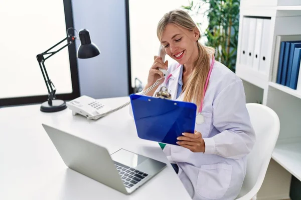 Young Blonde Woman Wearing Doctor Uniform Talking Telephone Reading Document — ストック写真