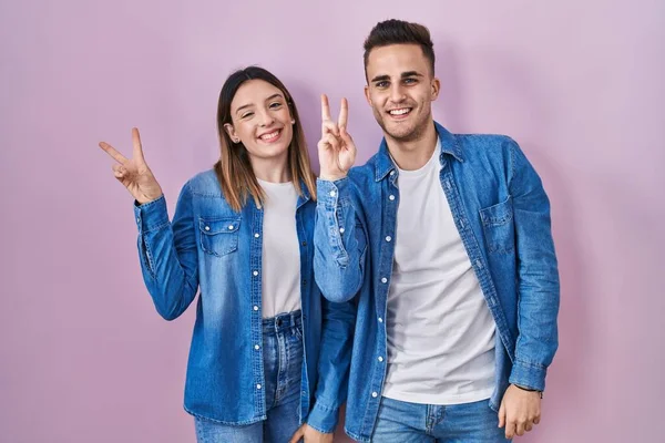 Young Hispanic Couple Standing Pink Background Smiling Happy Face Winking — Zdjęcie stockowe
