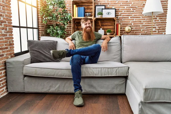 Young redhead man smiling confident sitting on sofa at home