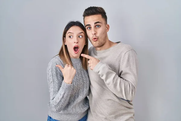 Young Hispanic Couple Standing White Background Surprised Pointing Finger Side — Photo