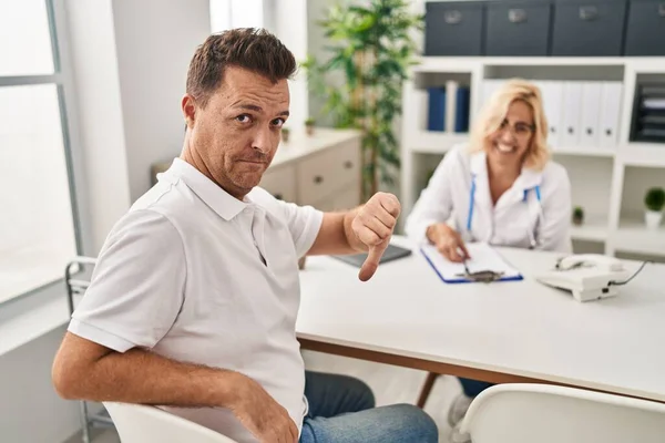 Hispanic man at the doctor with angry face, negative sign showing dislike with thumbs down, rejection concept