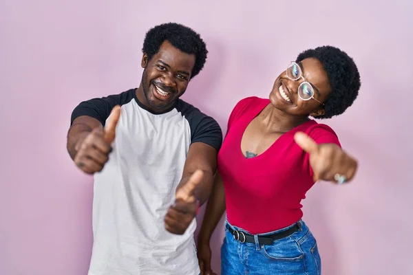 年轻的非洲裔美国夫妇站在粉红的背景上 赞成用手做积极的手势 微笑着竖起大拇指 为成功感到高兴 优胜手势 — 图库照片