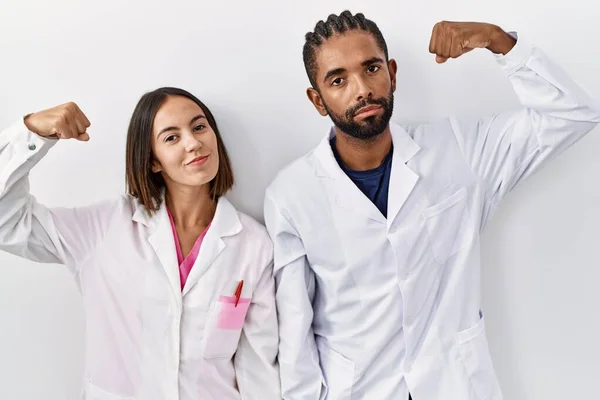Young Hispanic Doctors Standing White Background Strong Person Showing Arm —  Fotos de Stock