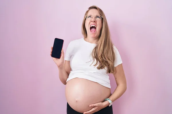 Mladá Těhotná Žena Ukazuje Břicho Drží Smartphone Naštvaný Šílený Křičí — Stock fotografie