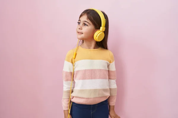 他的惊慌失措的小女孩用耳机侧身听音乐 用自然的脸和自信的微笑放松自己的姿态 — 图库照片