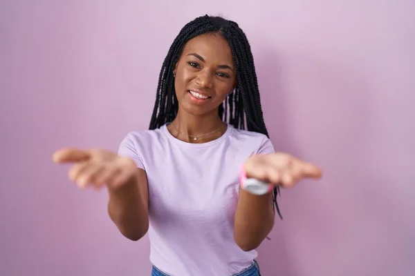Африканская Американка Косичками Стоящая Розовом Фоне Весело Улыбаясь Предлагая Руки — стоковое фото