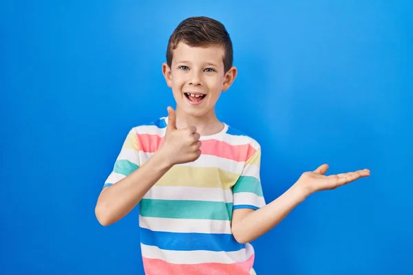 年轻的高加索小孩站在蓝色的背景上 手牵着手 竖起大拇指做手势 开心地微笑着 — 图库照片