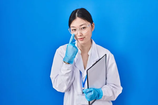 Chinese young woman working at scientist laboratory pointing to the eye watching you gesture, suspicious expression