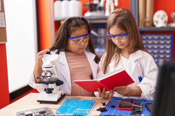 Two kids students using microscope reading notebook at laboratory classroom
