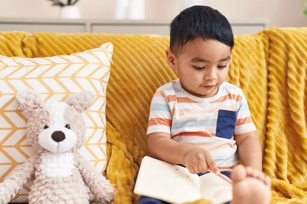 Adorable Hispanic Toddler Reading Book Sitting Sofa Teddy Bear Home — Stock Photo, Image