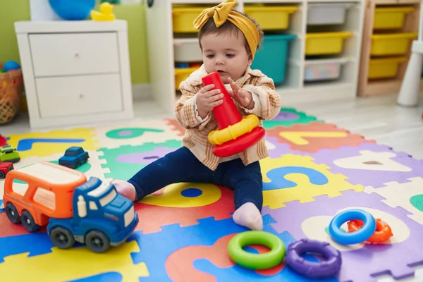 幼稚园里可爱的金发碧眼的幼儿抱着圈圈玩具坐在地板上 — 图库照片
