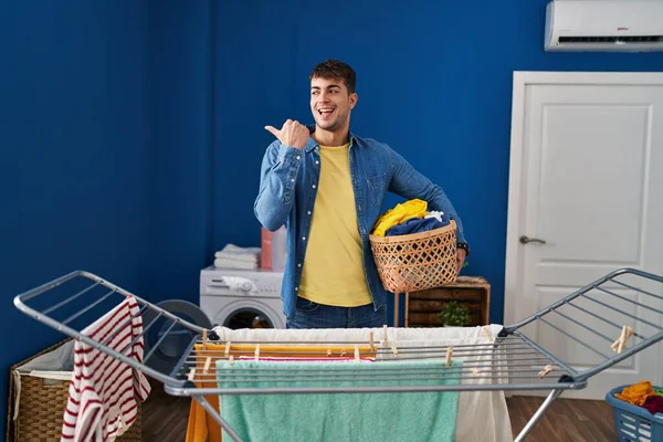 Young Hispanic Man Hanging Clothes Clothesline Pointing Thumb Side Smiling — Stock Photo, Image