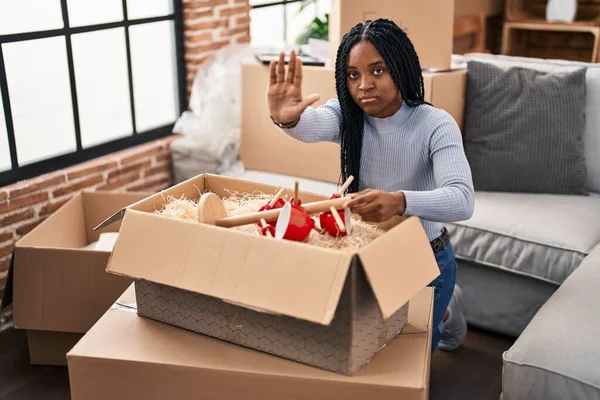 African american woman moving to a new home opening boxes with open hand doing stop sign with serious and confident expression, defense gesture