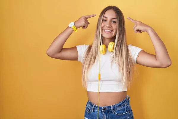 Young Blonde Woman Standing Yellow Background Wearing Headphones Smiling Pointing — ストック写真