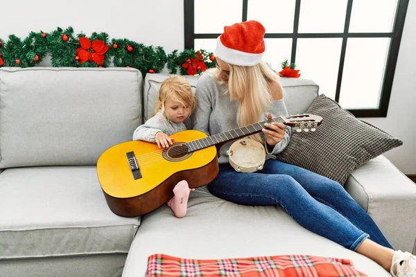 Mother and daughter playing guitar and tambourine sitting by christmas decor at home