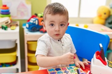 Adorable hispanic toddler playing with maths puzzle game sitting on table at kindergarten