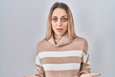 İzole edilmiş arka planda balıkçı yaka kazak giyen genç sarışın kadın hiçbir şeyden habersiz ve kolları açık, hiçbir fikri yok.. 