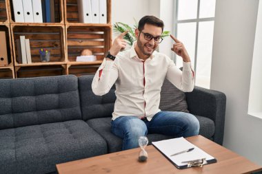 Young hispanic man with beard working at consultation office smiling pointing to head with both hands finger, great idea or thought, good memory 
