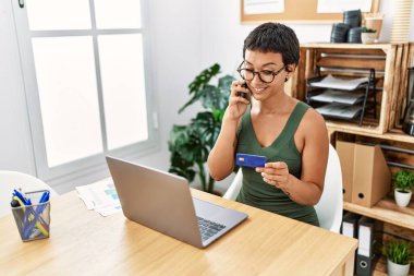 Ofiste kredi kartıyla konuşan Latin kökenli genç bir kadın.