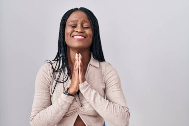 African woman with braids standing over white background begging and praying with hands together with hope expression on face very emotional and worried. begging. 