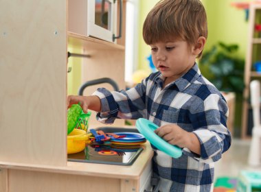 Adorable hispanic boy playing with play kitchen standing at kindergarten