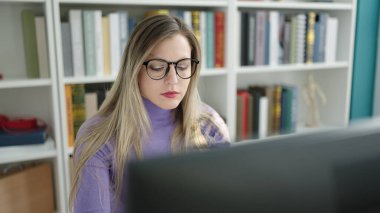 Young blonde woman student using computer studying at library university