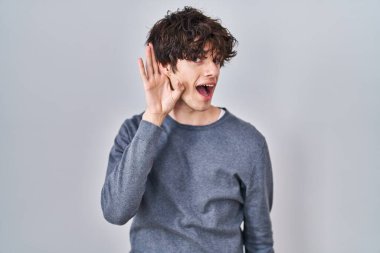 İzole edilmiş arka planda dikilen genç adam kulağına fısıldayarak dedikoduları ve dedikoduları dinliyor. Sağırlık kavramı. 