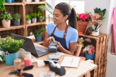 Young beautiful hispanic woman florist using laptop and data phone at florist