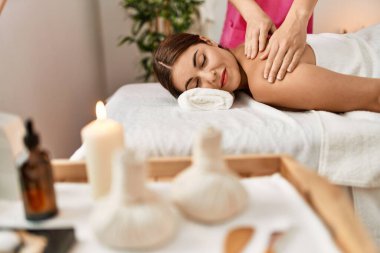 Young beautiful hispanic woman lying on table having back massage at beauty salon