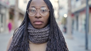 African woman standing with serious expression wearing glasses at street