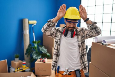 Young hispanic man with beard working at home renovation doing bunny ears gesture with hands palms looking cynical and skeptical. easter rabbit concept. 