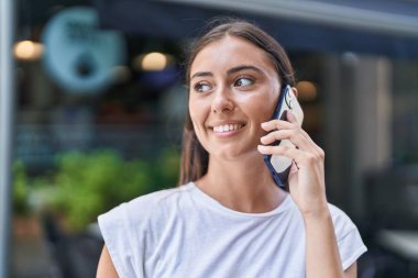 Genç, güzel İspanyol kadın, gülümsüyor. Kafe terasında akıllı telefondan konuşuyor.