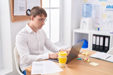 Ofiste çalışan genç beyaz bir iş adamı dizüstü bilgisayar kullanıyor.