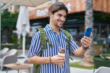 Young hispanic man tourist using smartphone eating ice cream at street