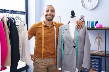 Genç Latin terzi gülümsüyor Atölyede kendine güvenen manikine yaslanıyor