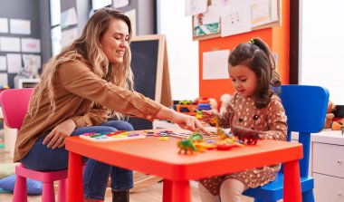 Teacher and toddler playing with maths puzzle game sitting on table at kindergarten