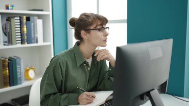 Young caucasian woman student using computer taking notes at library university