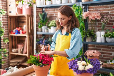 Young beautiful hispanic woman florist cutting plants at florist