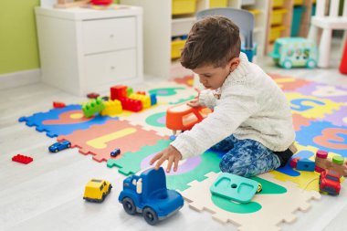 Tapılası İspanyol bebek arabalarla oynuyor. Anaokulunda yerde oturuyor.